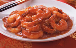 糖醋蝦菜餚，配上筷子，放在紅色圖案桌布上。 — 16:10 壁紙