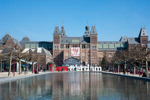 阿姆斯特丹國立博物館與「I am Amsterdam」標誌在陽光下倒映在水中。 — 博物館 壁紙