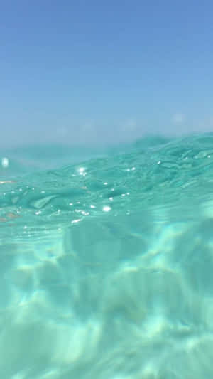 清澈碧綠的海水，帶有陽光反射和藍天在上 — 美學藍色 iPhone 壁紙