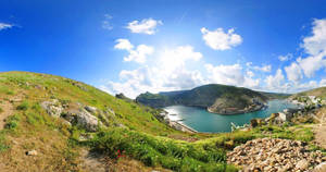 海岸海灣，有綠色山丘和小村莊，在明亮陽光下。