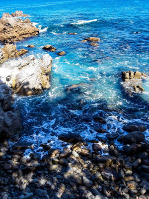 碧綠的海浪拍打岩石海岸，陽光下的鵝卵石閃閃發光。 — 海灘 壁紙