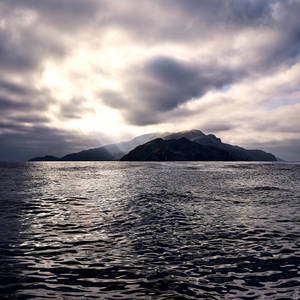 陽光穿透雲層，照亮平靜水面上的山島。 — macOS Catalina 壁紙