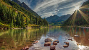陽光穿過雲層，照在寧靜的山間湖泊上，周圍環繞著常綠樹木。 — 湖泊 壁紙