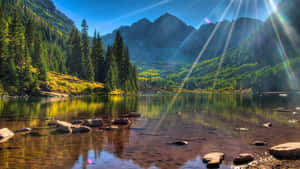 陽光穿過山峰，照耀在平靜的湖面上，周圍有森林和秋色。 — 科羅拉多落磯隊 壁紙