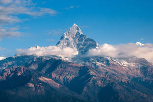 積雪的山峰聳立於雲層之上，下部山坡沐浴在金色的陽光中。 — 山脈 壁紙