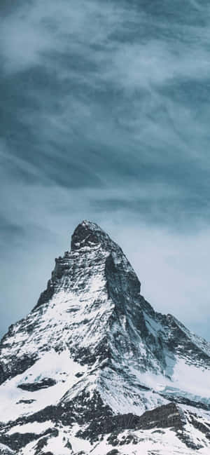 白雪覆蓋的山峰在冷藍色天空下穿過戲劇性的雲層升起。 — Valorant iPhone 壁紙