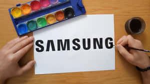人在白紙上用水彩畫Samsung標誌。 — 三星 壁紙