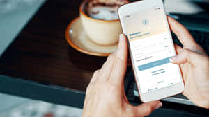 一個人在咖啡杯旁邊登入應用程式。 — 16:9 壁紙