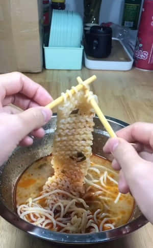 雙手用筷子從金屬碗中夾起冒煙辣味拉麵。 — Nubia Flip2 壁紙