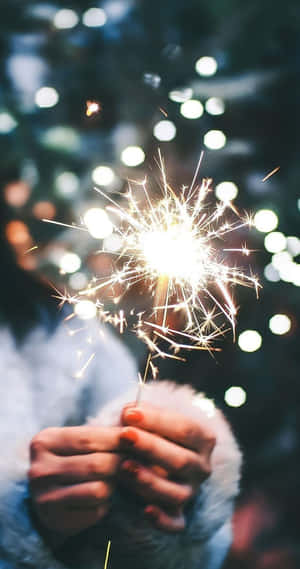 夜晚手持閃爍的煙火，背景有模糊的燈光。 — 新年快樂 壁紙