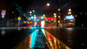 城市街道上的夜雨，模糊的交通燈光反射在濕漉漉的路面上。 — 黑暗城市 壁紙