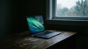 暗室中的MacBook，窗外下著雨，充滿氛圍感。 — Mac 壁紙
