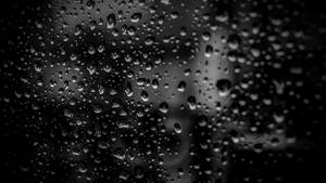 玻璃上的雨滴遮擋了模糊的灰階城市景觀。 — 黑色桌面 壁紙