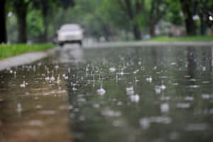 雨滴在濕路上飛濺，遠處有一輛模糊的汽車。 — 下雨 壁紙