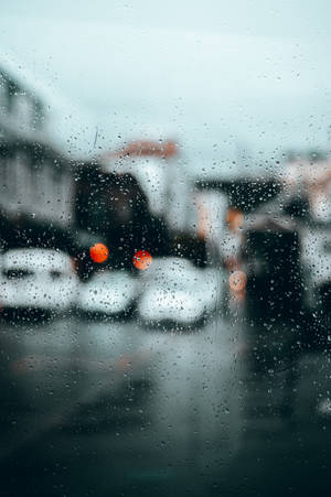 窗戶上的雨滴俯瞰著模糊的城市街道，帶有橙色車燈。 — 洗車 壁紙