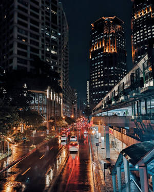 夜晚城市街道，濕漉漉的路面反射著車燈和高樓大廈。 — 城市燈光 壁紙