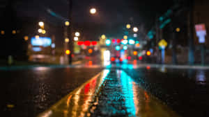 雨夜街道，模糊的燈光反射在潮濕的人行道和黃線上。 — 4K 桌布 壁紙