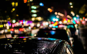 引擎蓋上的雨滴反射出夜晚多彩的城市燈光。 — 城市燈光 壁紙