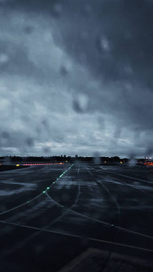 雨滴模糊了黑暗的機場跑道，在暴風雨的天空下，燈光閃爍發光。 — 伸展台 壁紙
