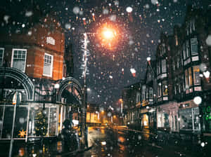 夜間潮濕的城市街道上飄雪，有發光的街燈和節日櫥窗。 — 寒冷 壁紙