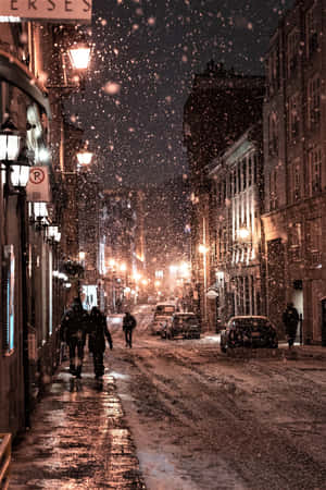 夜晚，雪落在溫暖照亮的城市街道上，人們在行走。 — Oppo Pad Mini 壁紙