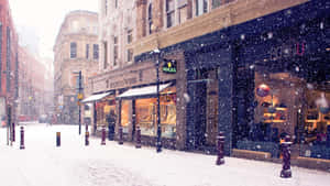 城市街道上飄雪，有明亮的商店櫥窗和歷史建築。 — 冬季風景 壁紙