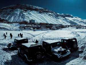 白雪覆蓋的山村，停放的吉普車和玩雪的孩子們。 — 山景 壁紙