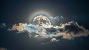 一輪滿月從縷縷雲絲後探出，帶有柔和的光暈效果。 — 月光 壁紙