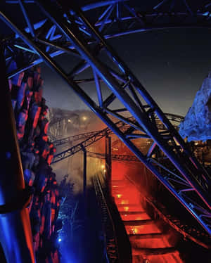 夜間以紅藍燈光照亮的雲霄飛車軌道，下方有薄霧。 — 4:5 壁紙