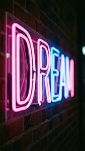 夜間在磚牆上發出粉紅色和藍色光芒的 DREAM 霓虹燈招牌。