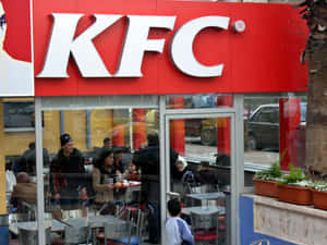 人們在帶有紅色標誌和玻璃窗的KFC餐廳內用餐。 — 肯德基 壁紙