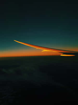 飛機機翼在雲層上方的橙色日落天空中呈現剪影。 — Kindle Paperwhite 壁紙