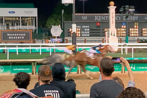 肯塔基德比夜間賽事，馬匹衝過終點線，人群觀看。 — 高解析度馬匹 壁紙