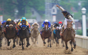 騎師在賽馬期間於泥濘的泥地上策馬奔馳。 — 賽馬 壁紙