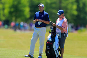 高爾夫球手 Bill Haas 和他的球童在陽光明媚的高爾夫球場上檢討策略。 — 運動 壁紙