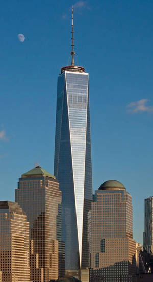 One World Trade Center摩天大樓，藍天中有月亮，周圍建築物沐浴在金色陽光中。 — 藍天 壁紙