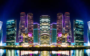 夜晚的城市天際線，燈火通明的摩天大樓倒映在水中。 — 莫斯科 壁紙