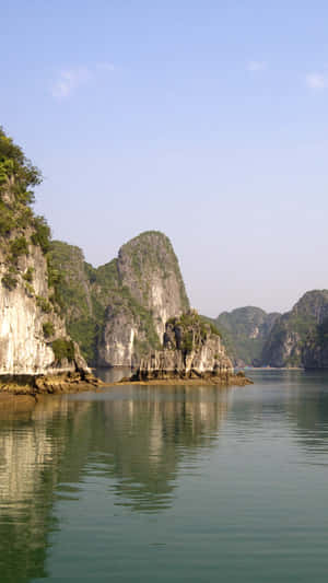寧靜的海灣，高聳的石灰岩喀斯特地貌倒映在平靜的碧綠海水中，天空晴朗湛藍。 — 島嶼 壁紙