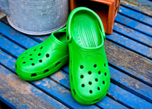 藍色木長凳上的亮綠色木屐，附近有園藝用品。 — Crocs 壁紙