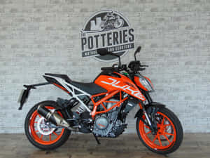 橙色KTM Duke機車在展示間中展出，背景為磚牆。 — 改裝摩托車 壁紙