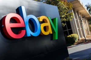 現代辦公大樓外色彩繽紛的eBay標誌招牌，有樹木和日光。 — eBay 壁紙