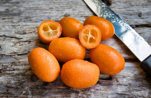 新鮮金橘在木質表面上切開，旁邊有刀。 — 柳橙 壁紙