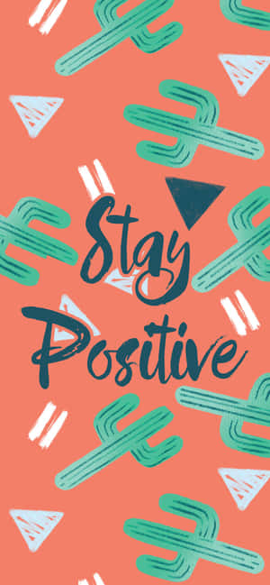 勵志短語 stay positive 被仙人掌和三角形圖案包圍在珊瑚色背景上 — Galaxy A35 壁紙