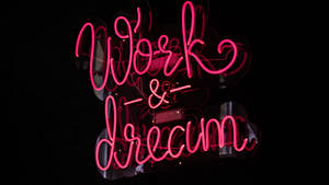 深色反光表面上寫著 Work & Dream 的粉紅色霓虹燈牌 — 霓虹紅 壁紙