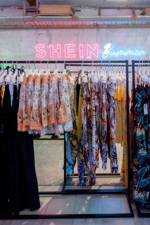 服裝店中SHEIN霓虹燈招牌下展示的彩色夏日連衣裙。 — 小米平板 9 Pro Max 壁紙