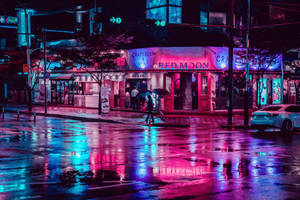 行人撐傘走過夜晚霓虹燈照亮的下雨城市街道。 — 城市燈光 壁紙