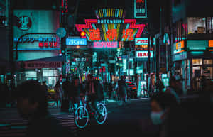 霓虹燈照亮夜晚的東京街道，有騎自行車者和行人。 — 暮光 壁紙