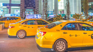 黃色的計程車在夜晚停放在繁忙的城市街道上，背景是明亮的建築物。 — 黃色 壁紙