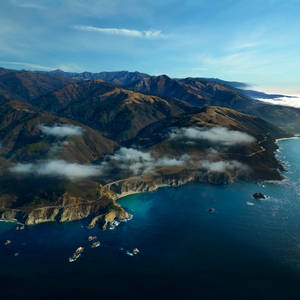 沿海公路沿懸崖蜿蜒，藍天下有海洋和山脈。 — 海洋桌面 壁紙
