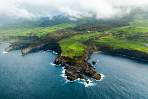 鳥瞰圖：綠色的梯田山丘和懸崖在雲下與海洋交匯。
